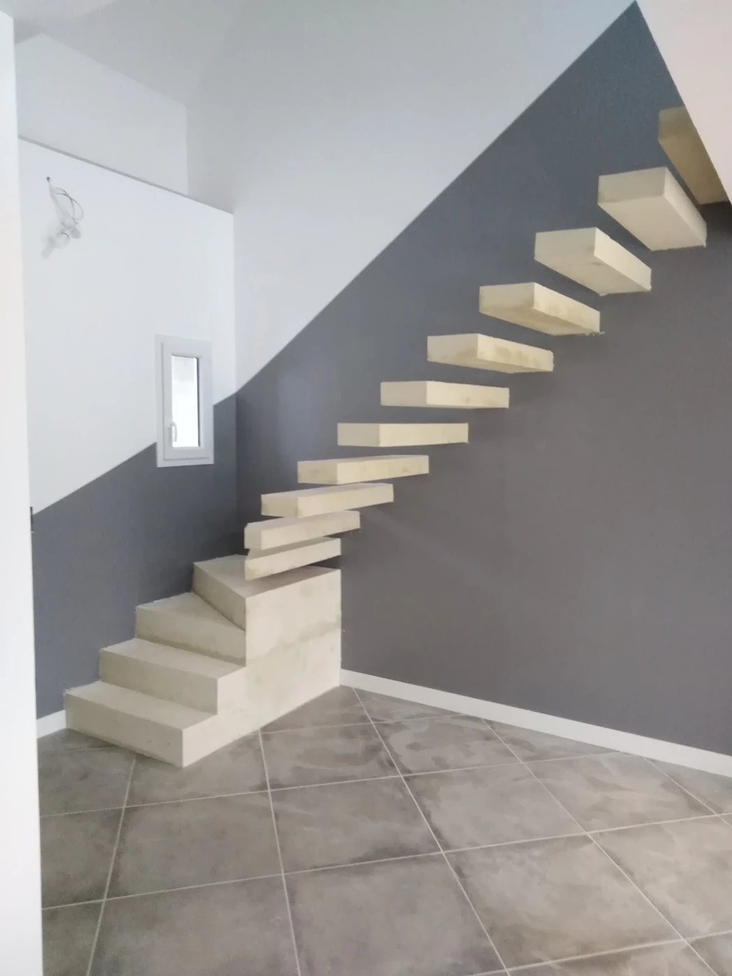 Escalier en béton aux marches suspendues, contre un mur gris